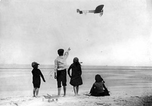 Right side long view from below and slightly to the rear of Blriot XI in flight; four children watch from beach in foreground. Original French caption: Le monoplan XI de Bleriot pique droit vers la cte anglaise. ["Blriot's monoplane XI heads right for the English coast." This would seem to indicate that the aircraft is being piloted by Louis Blriot himself.]